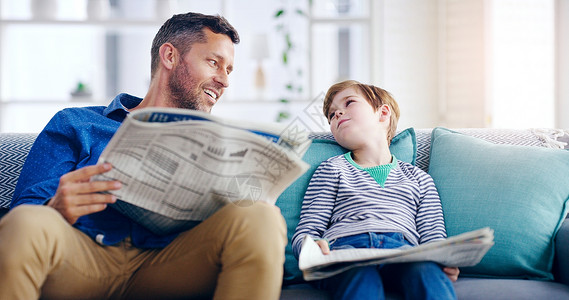 父子看报纸确保他知道知识就是力量 一对英俊的父子坐在家里的沙发上一起看报纸背景