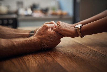 一对夫妇在家中的木制桌子上手牵手支持 悲伤和愈合 一位爱心伴侣因癌症而悲痛地关紧 并在家里表达同情之情;他背景图片