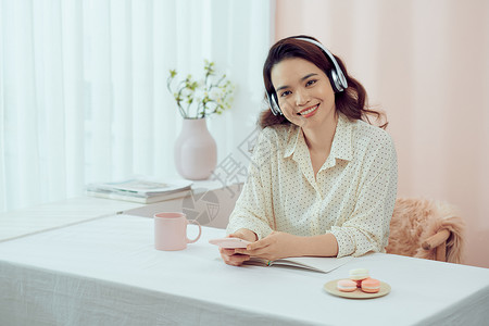 龙与音乐素材有吸引力的千年亚洲妇女在舒适的起居室放松 在阅读书时吃玛卡龙背景