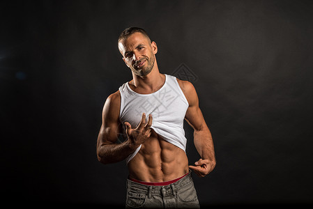 运动健壮的人抬起衬衫露出腹部男性背心肌肉腹肌工作室运动员优势黑色背景图片