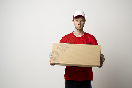 年轻送货员 穿红色制服的快递员 拿着大包裹在白色背景上导游高清图片素材