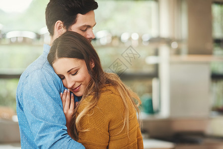 他们无可救药地相爱 一个可爱的年轻夫妇 拥抱在他们的厨房里背景