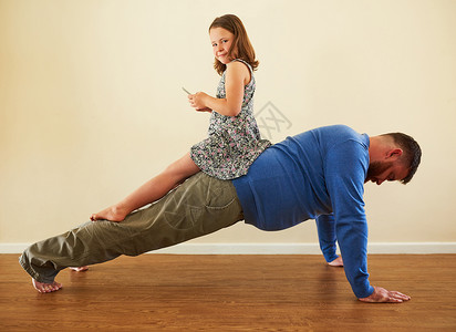 爸爸说 少打电话多健身 一个可爱的小女孩在父亲锻炼时背着他玩手机背景图片