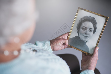 一位年长的女士看着一张黑白老相片 一个女人的旧照片 她写道背景