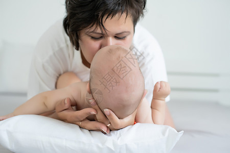 母亲和孩子在一张白色的床上 穿着尿布的妈妈和男婴在卧室里玩耍 父母和小孩在家里放松 一家人在一起玩得很开心拥抱毯子睡眠女孩母性房快乐的高清图片素材