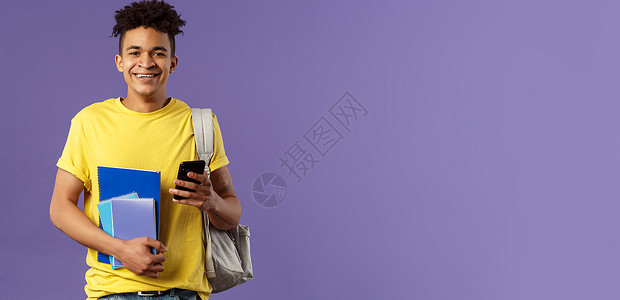回到学校 大学的概念 肩背背包 拿着笔记本和学习书籍 给朋友手机发短信的快乐年轻帅气男学生的画像教育爆炸职业紫色套装微笑家庭作业背景图片