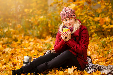 秋天妇女喝咖啡 秋季风景中 年轻女性从可支配咖啡杯享受热饮的概念落幕巧克力手套幸福帽子时尚咖啡叶子混血公园微笑背景图片