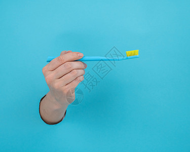 女人的手棍从蓝纸背景里拿出来 拿着牙刷工作室牙齿蓝色山峰手臂女性牙科保健纸板卫生背景图片