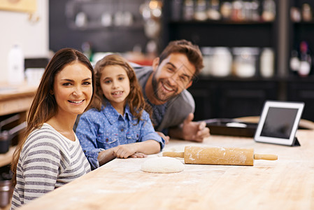 吃货你就来他们是一个吃货家庭 一个幸福的三口之家的肖像在厨房里一起烘烤 用数字平板电脑来帮助他们背景
