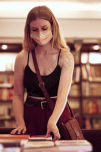 Covid 面罩和在图书馆 书店或教育大楼里拿着书的女人 以获取知识 阅读或研究 年轻女学生在书店桌上浏览和选择小说背景图片