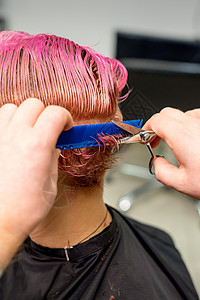 美发师在美发沙龙用梳子梳理年轻白人女性染成湿粉红色的短发粉色成人修剪理发店发型师顾客剪刀造型师职业客户女士高清图片素材