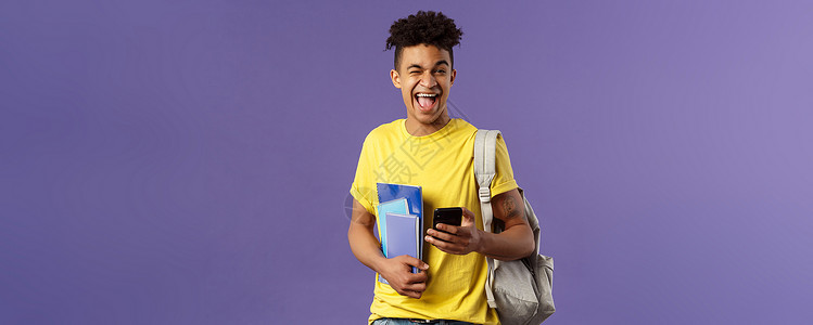 回到学校 大学的概念 快乐 微笑的快乐男人 使用手机的学生 乐观地对着镜头眨眼 拿着背包和笔记本 讲座笔记和智能手机理发紫色校园背景图片