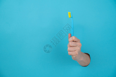 女人的手棍从蓝纸背景里拿出来 拿着牙刷蓝色卫生塑料女性工作室裁剪纸板保健牙科山峰背景图片