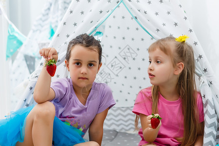 两个小女孩在家里吃草莓 在假发帐篷附近吃草莓棚屋乐趣婴儿姐姐童年女性早餐小吃浆果水果太阳高清图片素材