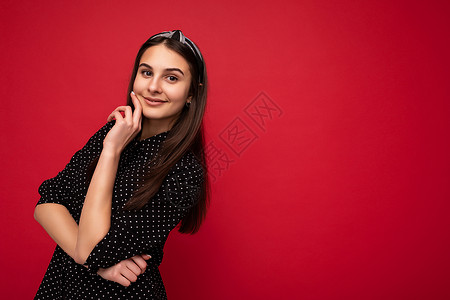 年轻迷人 美丽 快乐 微笑的黑发女人的肖像照片 她身穿黑色圆点衬衫 在红色背景上与空旷的空间隔开 情绪真挚背景图片