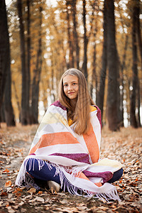 美丽的年轻女孩坐在地上 满是黄叶子 在秋天的森林里背景图片
