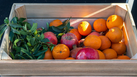 石榴包装和太阳光下的木箱中的橙子和石榴土背景