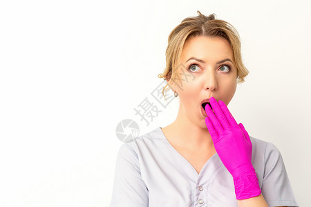 一位年轻的天主教女医生或护士的肖像被用粉色手套手在白色背景上蒙住嘴而震惊 笑声化妆师耻辱女士专家秘密外科成人女性女孩惊喜安静高清图片素材