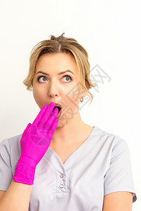 一位年轻的天主教女医生或护士的肖像被用粉色手套手在白色背景上蒙住嘴而震惊 笑声秘密手势女士工作冒充女性工作室成人外科惊喜担心高清图片素材