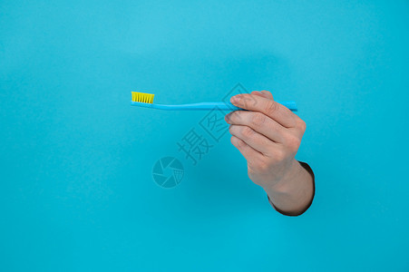 女人的手棍从蓝纸背景里拿出来 拿着牙刷女性工作室休息卫生手臂牙齿裁剪纸板蓝色塑料背景图片