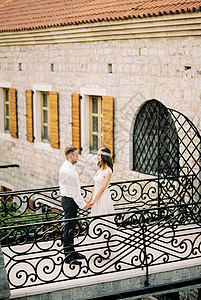 新娘和新郎站在旧石头大楼附近的桥上手牵手高清图片