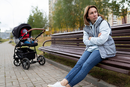 心烦的母亲坐在一张长凳上 把孩子和婴儿分开开来 这是产后抑郁症的概念沮丧高清图片素材
