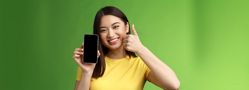 小朋宇吃西瓜特写满足可爱的亚洲女孩给予积极反馈 竖起大拇指显示智能手机屏幕 介绍很棒的新应用程序 推荐好的应用程序 在游戏中吹牛打分旅游女朋背景