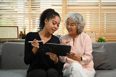 在沙发上一起在数字平板电脑上浏览互联网的微笑 重审的妇女及其孙女们 退休 技术概念轻松高清图片素材