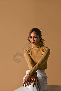 时尚工作室照片 秋冬概念 穿着时装毛衣 坐在棕色工作室背景上迷人的年轻女子背景图片