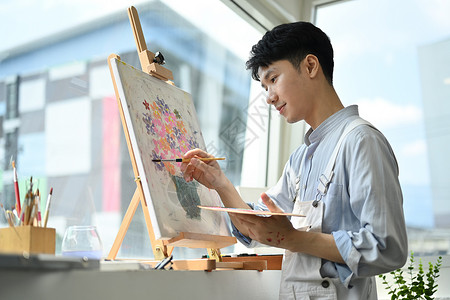 照片来自亚裔男性艺术家 在明亮的艺术演播室持纸笔和调色板画背景图片