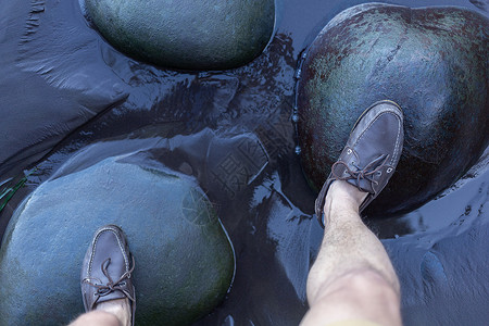 雄脚在水面上的绿色石頭上运动冒险靴子男人鞋类石头平衡黑色活动远足背景图片