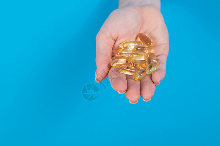 一个女人拿着一小撮3粒蛋白类的药片 一个手棍从一个洞里拿出来 在纸板蓝色背景下棕榈药品制药诊所药店化学品手指保健化学抗生素背景图片