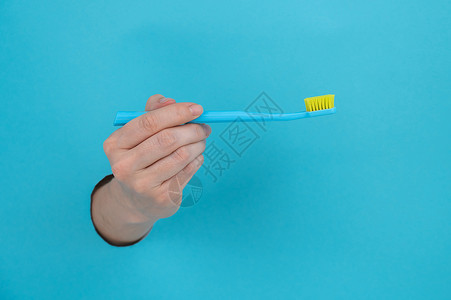 女人的手棍从蓝纸背景里拿出来 拿着牙刷卫生裁剪保健山峰休息女性塑料女孩牙科手臂背景图片