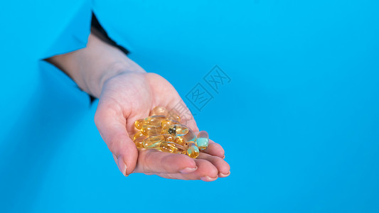 一个女人拿着一小撮3粒蛋白类的药片 一个手棍从一个洞里拿出来 在纸板蓝色背景下处方剂量症状化学品医院抗生素流感制药诊所治疗背景图片