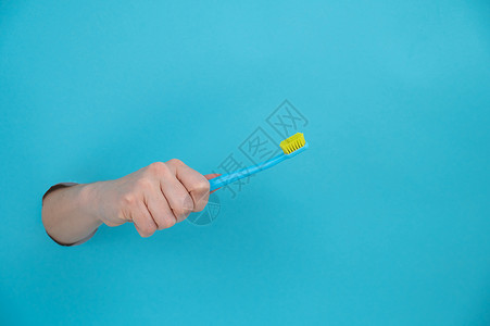 女人的手棍从蓝纸背景里拿出来 拿着牙刷牙齿卫生女孩山峰保健纸板蓝色女性裁剪手臂背景图片