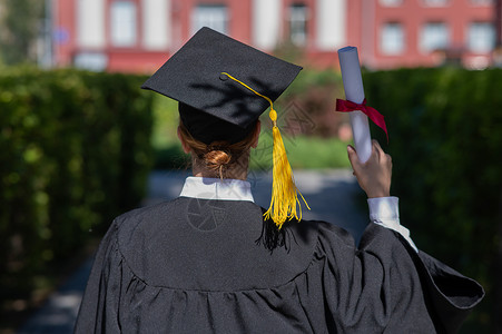 一位身着毕业礼服的天主教妇女带着一张有文凭的包裹站在大学附近 重现了她的视线幸福研究生证书蓝色成就教育裁剪传统学校帽子女性高清图片素材