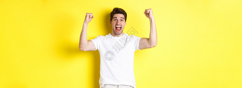 激动人心的男子获胜 举起手来庆祝 为团队赢得胜利和扎根 站在黄色背景之上的画面手势成功工作室潮人商业优胜者情绪胡须学生成人背景图片