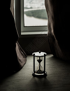 银色沙漏或沙玻璃放在房间的玻璃窗上小时窗户生活倒数手表窗台玻璃火焰晨光窗帘背景图片