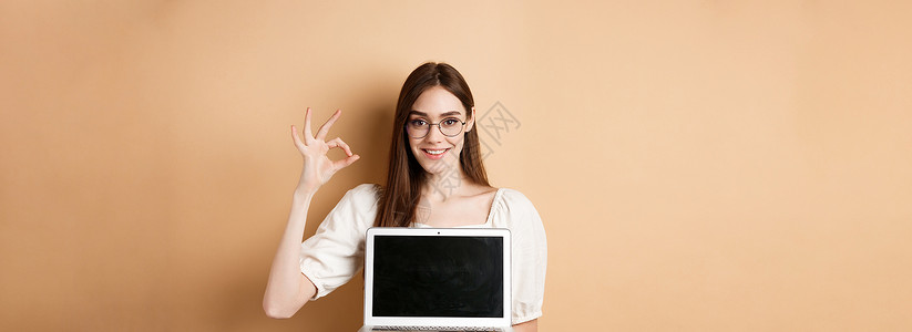 澳门回归20周年宣传展板电子商务 戴着眼镜的微笑的年轻女性显示出好的标志和笔记本电脑屏幕推荐米色背景上的互联网宣传化妆品褐色工作室技术周年纪念日自由职业背景
