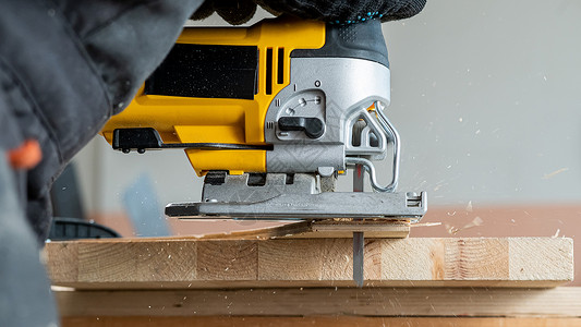 一名男子在车间用电锯砍木板的缝合装置上材料裁剪机器木头家具木材男性工匠锯末活动乐器高清图片素材