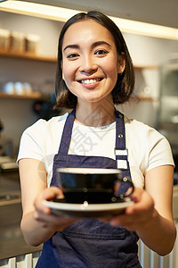 友好的亚洲女孩的垂直照片微笑着 端咖啡 咖啡师给你一杯咖啡 在咖啡馆里为客户准备饮料店铺职业成人杯子职员餐厅食堂人士咖啡店柜台日本人高清图片素材