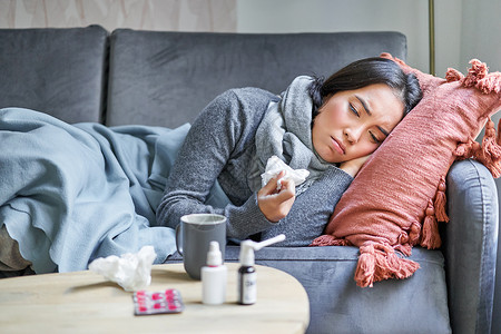 生病 悲伤的韩国女人躺在沙发上 感觉身体不适 感冒 流感和体温升高 看起来心烦意乱 正在服药药品温度毯子成人弱点过敏女性发烧感染房子高清图片素材