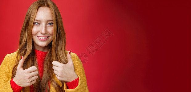 特写 穿着黄色外套 满意 快乐的 20 多岁年轻女性竖起大拇指表示赞同 给予积极反馈 享受站在红色背景下的美好活动 微笑可爱理发背景图片