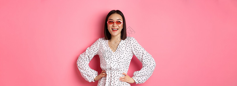 美丽的韩国妇女度假 戴墨镜和着装 笑笑微笑 站在粉红背景上 Y LA KF 女性青少年女孩冒充皮肤工作室横幅情感旅游理发快乐背景图片