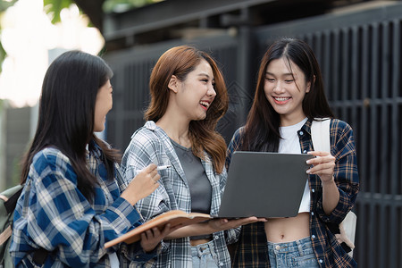 有朋友的美丽的年轻亚裔女大学生在户外 在大学校园工作的大学生阅读班级微笑电脑休闲装快乐男性背包男人女孩背景图片