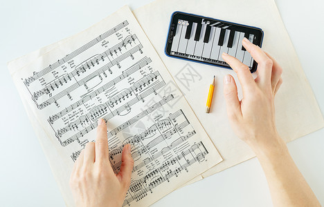 手机钢琴素材乌克兰利沃夫 — 2022 年 12 月 13 日 电话上弹钢琴 钢琴乐谱的节目 纸上的音符 智能手机上的程序 练习 从上面看背景