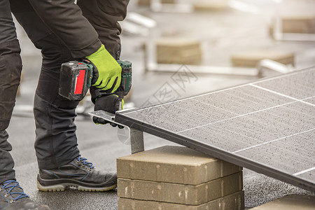 太阳能电池板安装人员使用铝制紧固件和无绳电钻将模块拧在一起 屋顶安装工作和安全 带复制空间的概念活力力量生态钻头房子蓝色技术工人背景图片