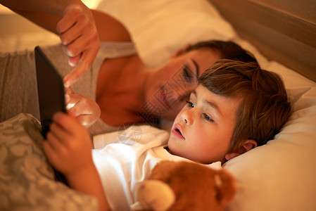 不想理你表情包你想不想读这个故事? 一个母亲和儿子躺在床上时 一起使用数字平板电脑背景