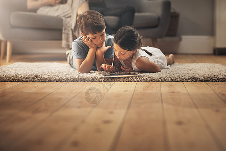 与数字玩具一起成长 一对可爱的兄妹在家里使用数字平板电脑 背景是他们的父母男性高清图片素材