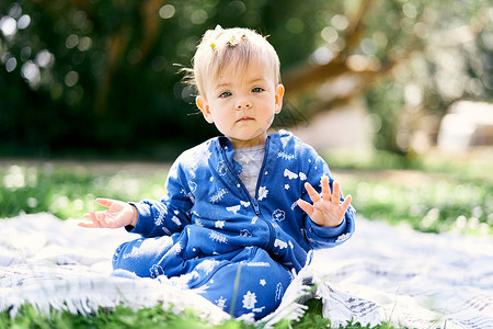 穿着蓝制服的小孩坐在绿草坪上的毯子上 用绿树背景展示他的手掌背景图片
